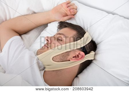 Young Handsome Man Sleeping With Anti Snoring Chin Strap On Head At Home