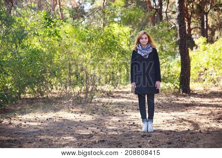 Beautiful, young girl in a dark coat, in a scarf standing in a park on a sunny day