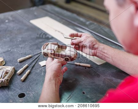 Master in a red uniform closeup of various tools collects a wooden model of a car