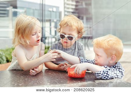 Group portrait of three white Caucasian cute adorable funny children toddlers sitting together sharing food. Love friendship childhood concept. Best friends forever