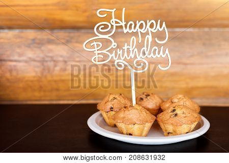 Birthday cakes and muffins with wooden greeting sign on rustic background. Wooden sing with letters Happy Birthday and holiday sweets