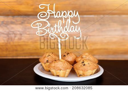 Birthday cakes and muffins with wooden greeting sign on rustic background. Wooden sing with letters Happy Birthday and holiday sweets