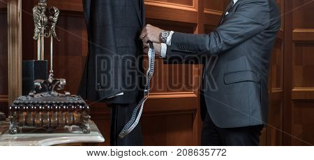 The tailor works with the dummy, measuring the costumes. Hands of a tailor man in suit in the interior of the boutique tailoring of individual suits