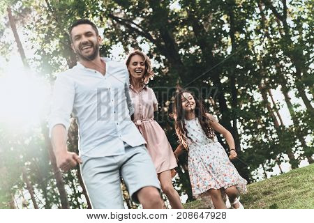 Strong family bonds. Happy young family of three holding hands and smiling while running in park