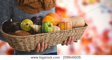 Mid section of woman holding fruits and vegetables in basket against view of maple leaves