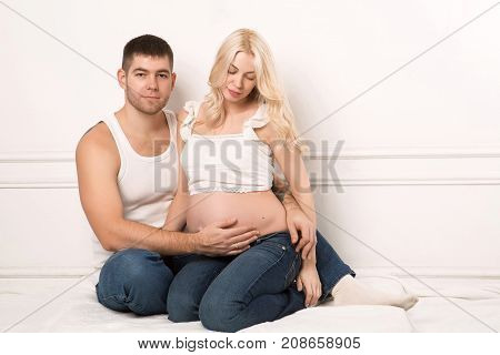 Beautiful pregnant couple in love on the background. Hands of husband on the tummy of his pregnant wife. Young man tenderly stroked pregnant belly of his wife. Husband kissing pregnant belly.