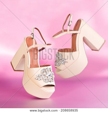The pair of beautiful beige sexy high sandals on a pink background. Women's high sandals soar above table on pink background