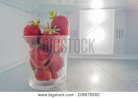 Glass full of red ripe strawberries stands on the shelf of fridge