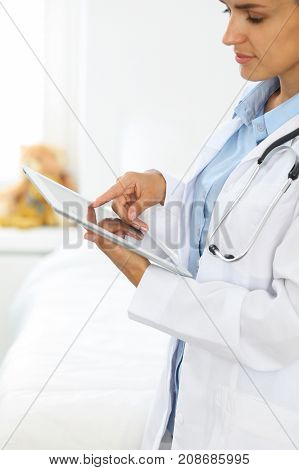 Woman doctor using tablet computer while standing straight in hospital.