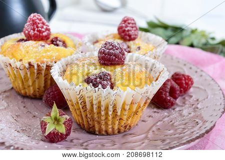 Delicious curd muffins with fresh raspberries decorated with powdered sugar on a ceramic plate.