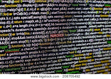 Macro photo of computer screen with program source code and highlighted HIJACKER inscription in the middle. Computer script on the screen with virus in it. Cyber security concept.