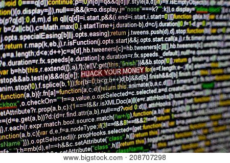 Macro photo of computer screen with program source code and highlighted HIJACK YOUR MONEY inscription in the middle. Computer script on the screen with virus in it. Cyber security concept.