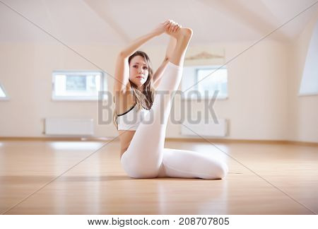 Beautiful woman practices yoga seated asana Kraunchasana in the yoga studio.