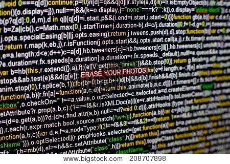 Macro photo of computer screen with program source code and highlighted ERASE YOUR PHOTOS inscription in the middle. Computer script on the screen with virus in it. Cyber security concept.