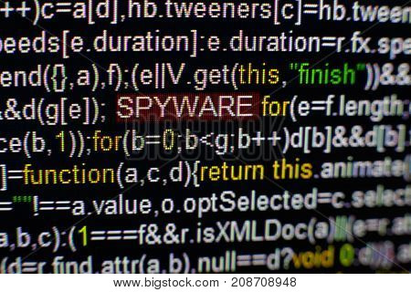 Macro photo of computer screen with program source code and highlighted SPYWARE inscription in the middle. Computer script on the screen with virus in it. Cyber security concept.