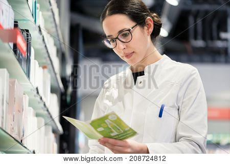 Low-angle portrait of an experienced female pharmacist checking the medical prescription of a pharmaceutical drug, while working in the interior of a modern drugstore with various products