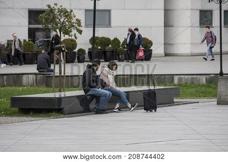 Galeria Krakowska square Cracow Poland - October 13 2017: Couple sitting on a black stone bench she have black suitcase on Galeria Krakowska square Cracow Poland.