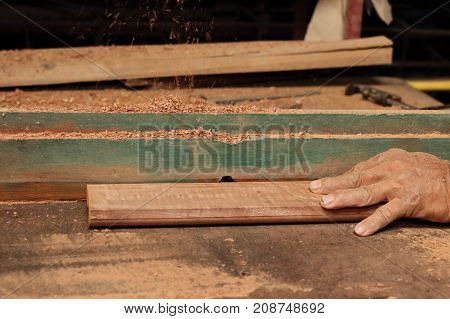 Hands of senior carpenter shaving a piece of wood on router table in carpentry workshop.