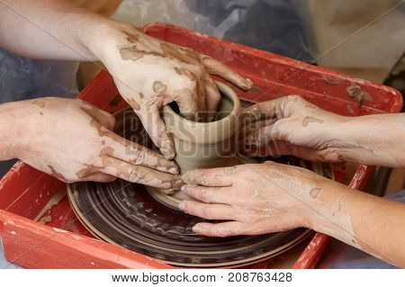 Hands of two people create pot on potter's wheel. Teaching pottery carftman's hands guiding