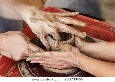 Hands of two people create pot on potter's wheel. Teaching pottery carftman's hands guiding