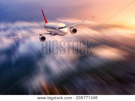 Modern airplane mith motion blur effect is flying over low clouds at sunset. Landscape with passenger airplane, blurred clouds, sunlight in dusk. Passenger aircraft. Business travel. Commercial plane