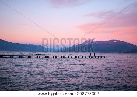 Romantic violet sunset on a lake with a long pier and a couple strolling by
