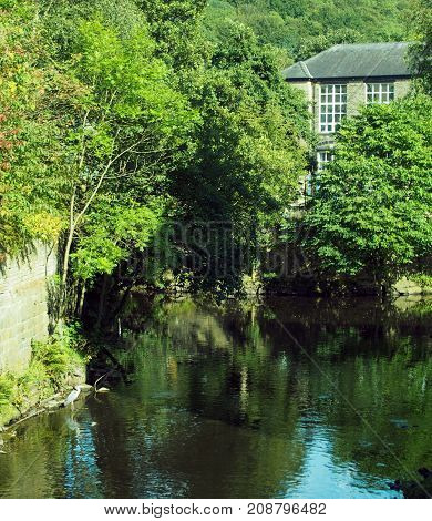the river calder jpoining the smaller river in hebden bridge with trees houses and a heron in the water