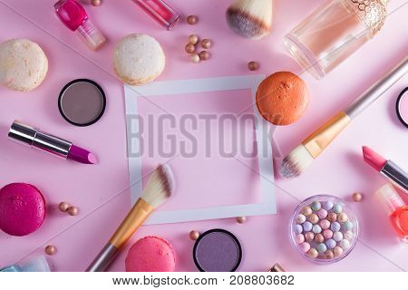 Make up products and macaroons frame with copy space on pink background