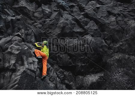 male rock climber. rock climber climbs on a black rocky wall on the ocean bank in Iceland, Kirkjufjara beach. man makes hard move without rope.