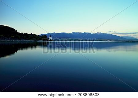 Mirroring on the water surface of Liptovska Mara at dusk. Water level, mirroring, blue sky and West tatras mountains. Beautiful Slovakia.
