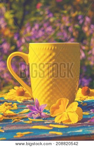 yellow сup with tea or coffee multicolor flowers around