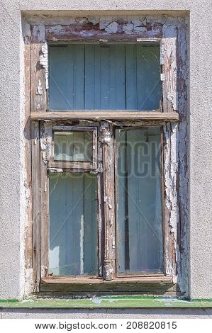 Old wooden window with a vent pane and the remains of white paint on the wall