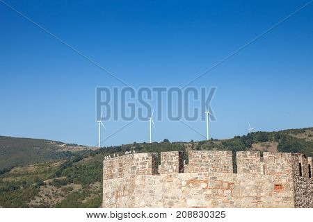 Romanian Wind Farm with Wind Turbine and windmills facing an old castle located on the Serbian side of the Danube river in the Iron Gates valley.