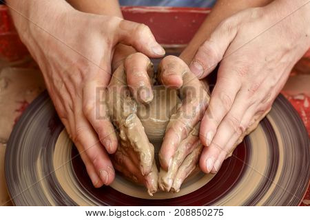 Hands of two people create pot on potter's wheel. Teaching pottery carftman's hands guiding