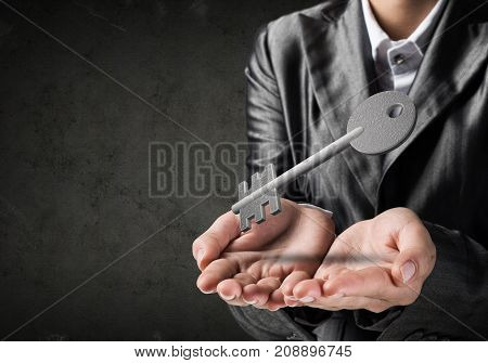 Cropped image of businessman in suit keeping stone key symbol in hands with dark wall on background. 3D rendering.