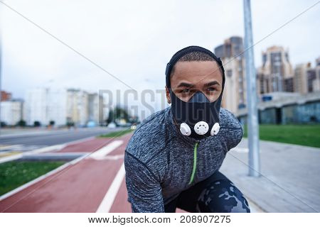 Athletic excellence. Close up shot of handsome young dark-skinned male runner about to start his run on track field using training mask to get better results while exercising outdoors in the morning