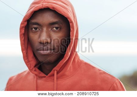 Portrait of a focused young African man in a hoodie standing with his eyes closed on a trail by the ocean preparing for a run
