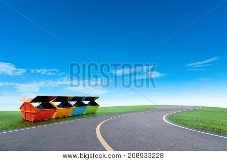 Colorful Industrial Waste Bin (dumpster) for municipal waste or industrial waste on green grass field and asphalt road blue sky backgroundwith ecology concept
