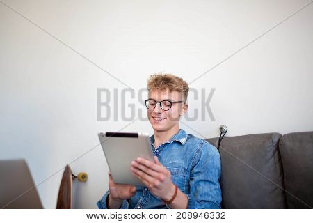 Smiling man skilled developer sites working on touch pad and laptop computer, sitting in co-working space. Young cheerful male website content creation using digital tablet and portable net-book