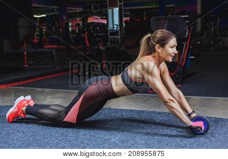 Slim bodybuilder girl does the exercises with Ab Wheel in the gym. Sports concept fat burning and a healthy lifestyle.