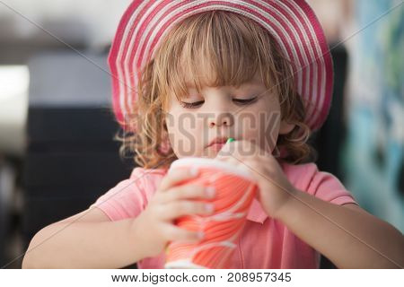 Adorable little girl drinking from glass with straw wearing straw hat summer vaccation.