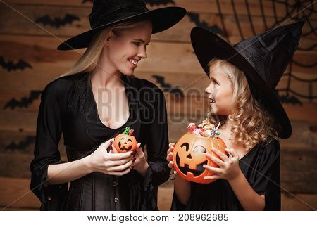 Halloween Concept - beautiful caucasian mother with disappointed feeling with happy little daugther enjoy with Halloween candy and sweet over bats and spider web on Wooden studio background.
