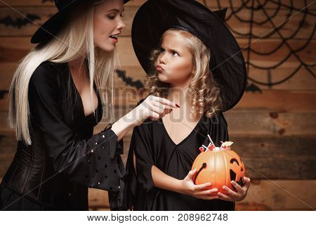 Halloween Concept - beautiful caucasian mother playing with her little daugther enjoy with Halloween candy and sweet over bats and spider web on Wooden studio background.