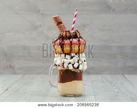 Chocolate and donuts extreme milkshake with marshmallow and other sweets in mason jar on gray wooden background. Crazy freakshake on gray wooden table with copy space