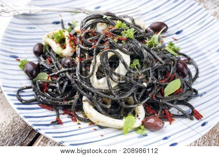 Italian linguine con tinta de calamari with olives as close-up on a plate 