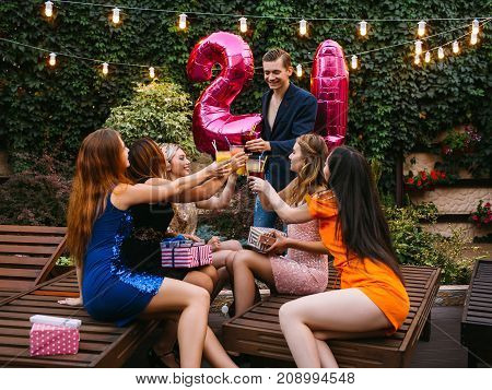 Friends company at birthday 21st party. Happy celebration in atmospheric place outdoors, adulthood for male. Joyful toast with beverages, congratulation concept