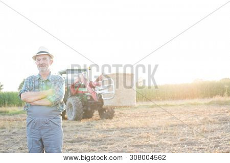 Senior farmer standing at fielf against tractor