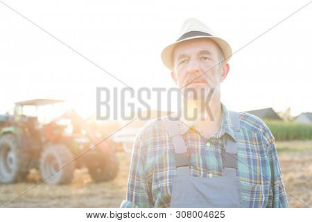Senior farmer standing at fielf against tractor