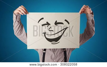Casual person holding a paper with cool emoticon in front of his face