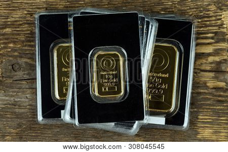 Several Gold Bars Of Different Weight In Plastic Packaging On A Wooden Background.